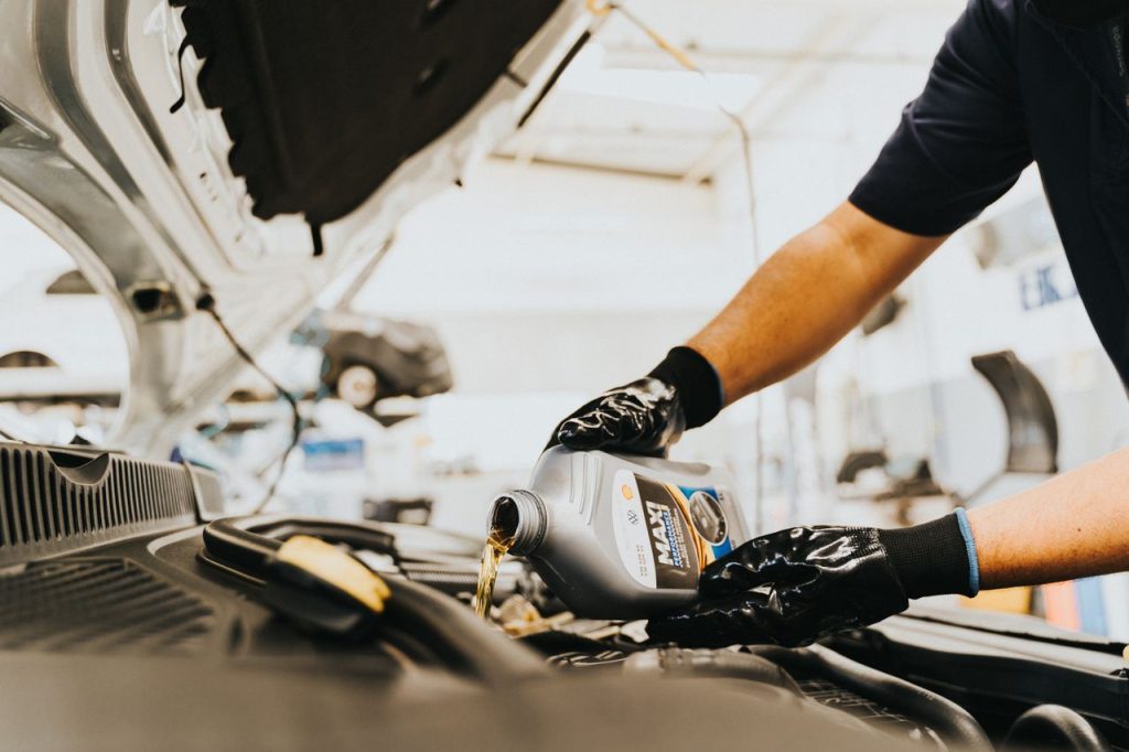 pexels photo 13065696 Close-up of a mechanic pouring engine oil in a car inside a garage. Hands wearing gloves.