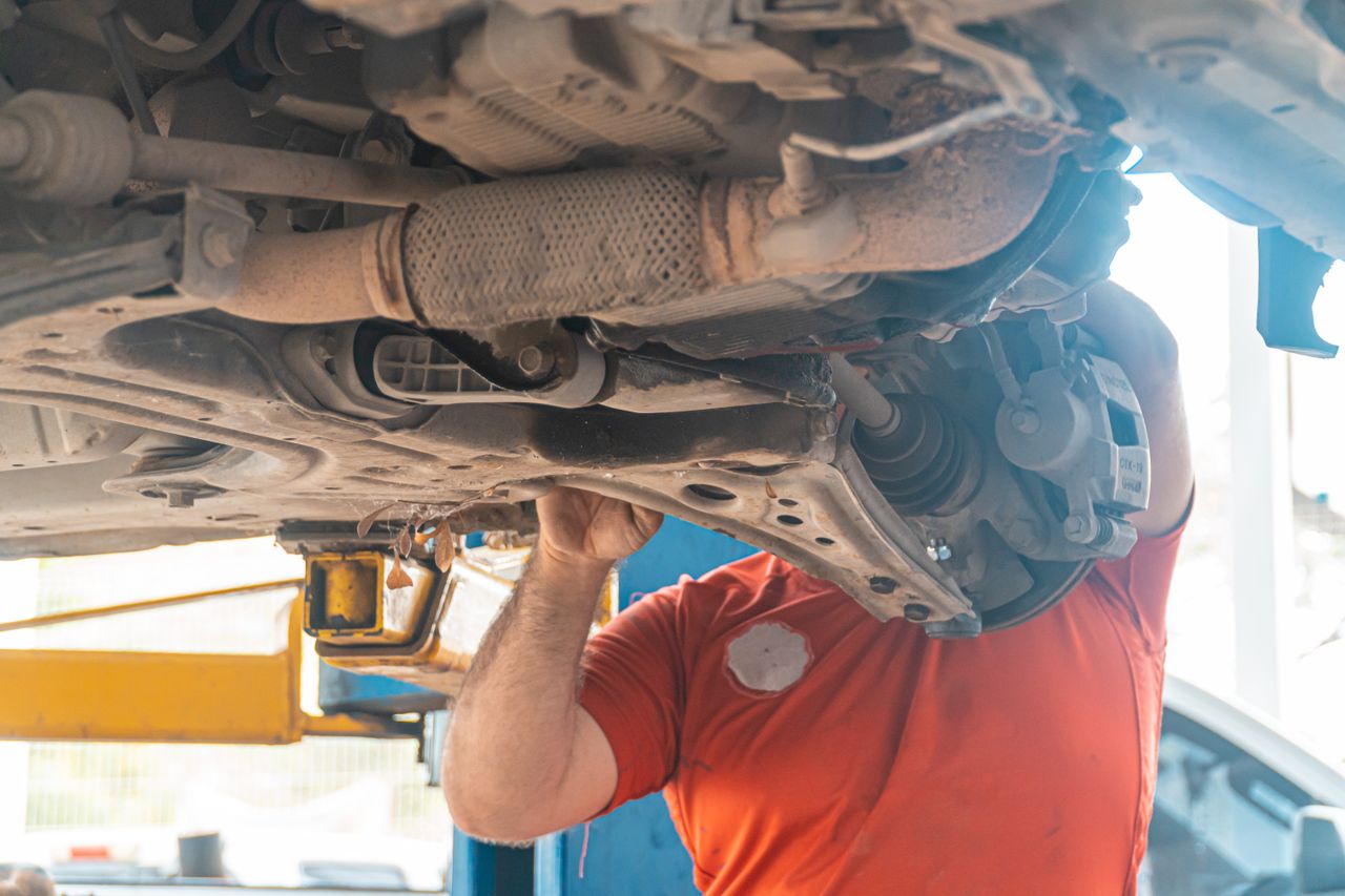Crafting Captivating Headlines: Your awesome post title goes here Mechanic working under a vehicle, inspecting the undercarriage in a repair garage, ensuring safety and performance.